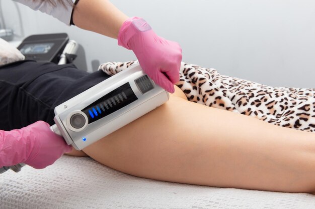 De masseur doet een massage met behulp van een anticellulitis-massageapparaat met compressie- en vibratietechnologie in het schoonheidssalon