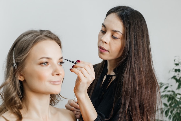 De meester doet een mooie blonde make-up in een schoonheidssalon