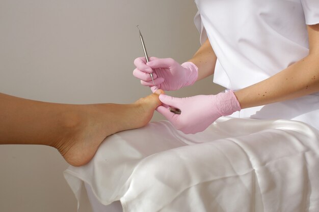 De meester in roze handschoenen maakt een pedicure op het been van de vrouw. Hoge kwaliteit foto