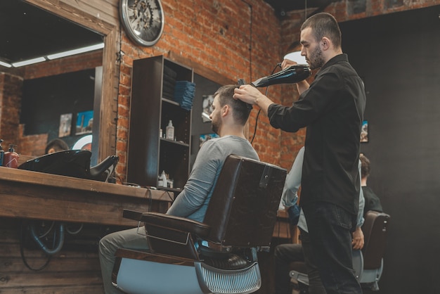 De meester van de Barbeshop blaast het haar en de baard naar de klant met een haardroger. Haar en baarden wassen. Kapper voor heren.