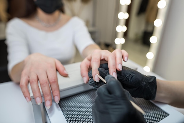 Foto de meester van de manicure zaagt en bevestigt een nagelvorm tijdens de procedure van nagelverlengingen in de schoonheidssalon professionele zorg voor handen