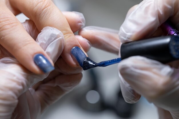 De meester van de nagelservice maakt een manicure close-up nagels waarop een blauwe gellak wordt aangebracht