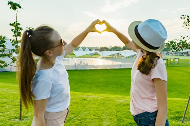 De meisjes tonen handen op hart op zonsondergangachtergrond