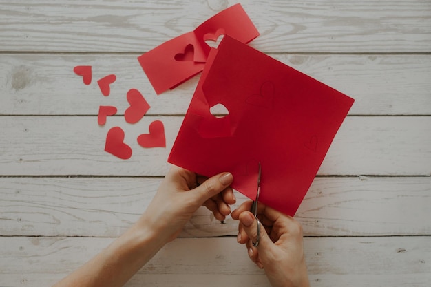 De meisjeshanden sneden harten uit rood papier boven een houten tafel Harten voor Valentijnsdag
