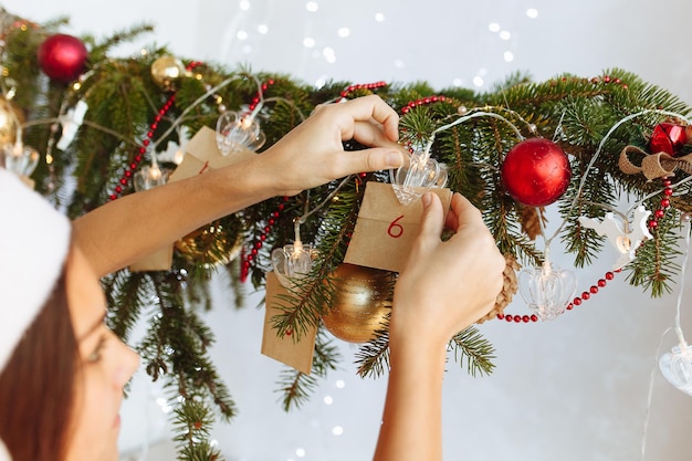 de meisjeshanden worden opgehangen aan de versierde tak van de adventskalender van de kerstboom diy