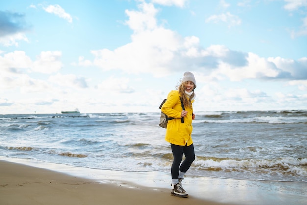 De meisjestoerist in een geel jasje die zich voordeed aan de zee Reizend levensstijlavontuur