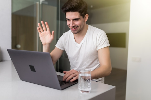 De mens communiceert op afstand via een videogesprek van een laptop die lacht en met zijn hand zwaait terwijl hij thuis is