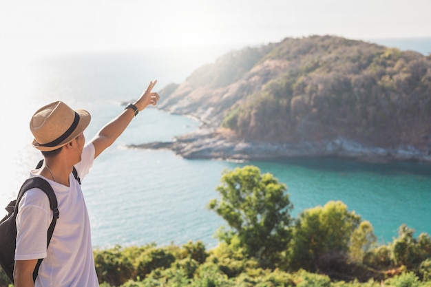 De mens die hoed draagt houdt zijn hand gelukkig. man aziatische toerist kijk naar bergen en de zee voor zonsondergang. voor activiteit levensstijl buitenshuis vrijheid of reizen toerisme inspiratie backpacker toerist naar covid 19