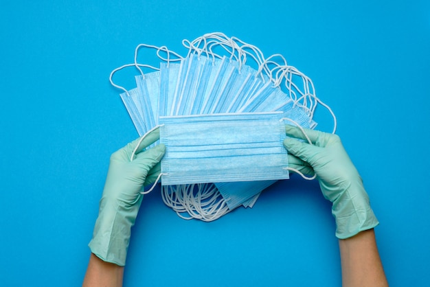 De mens dient beschermende handschoen in die gezichts beschermende maskers op blauwe muur houdt