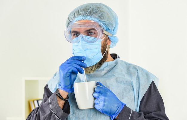 De mens drinkt koffie in een beschermend masker. uitbraak van een coronaviruspandemie. Arts ademen ademhalingsmasker. Ziekenhuis of vervuiling beschermen gezichtsmaskering. medisch masker als corona-bescherming.