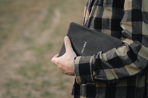 Foto de mens houdt de heilige bijbel buiten op een wazige groene achtergrond, geloof, spiritualiteit en religie