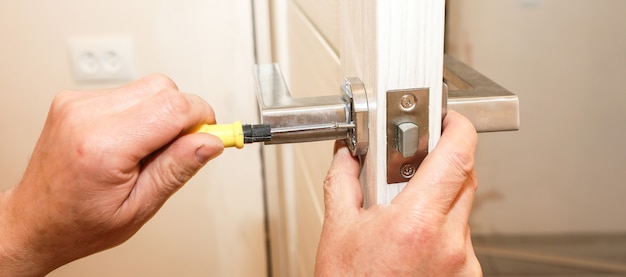 De mens installeert de deurklink. reparatie werkt. onderhoud in het appartement.