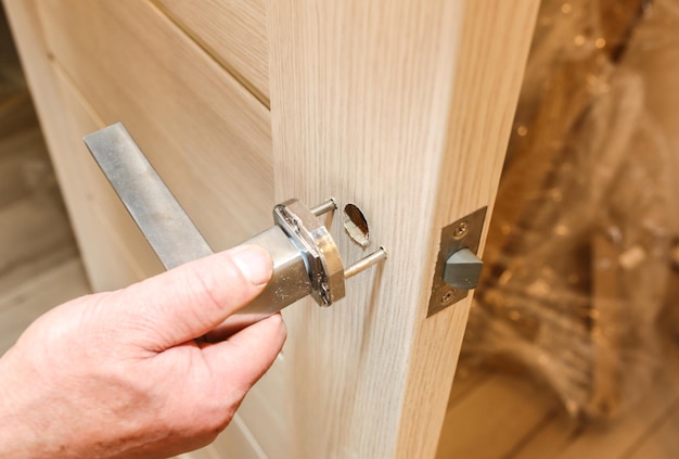 De mens installeert de deurklink. Reparatie werkt. Onderhoud in het appartement.