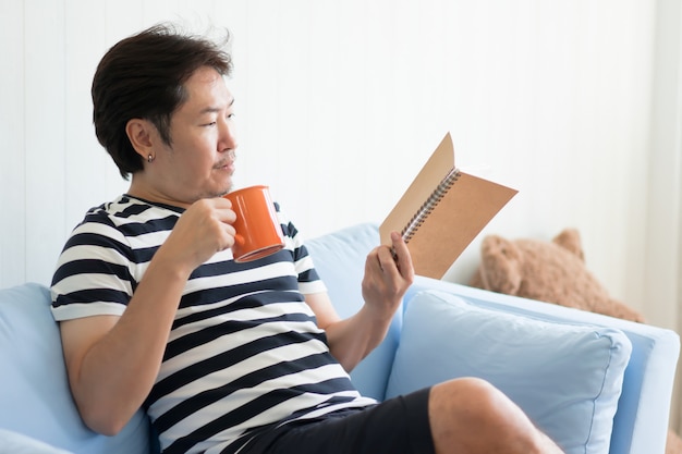 De mens met een mok en het lezen van een boek om thuis in woonkamer te ontspannen