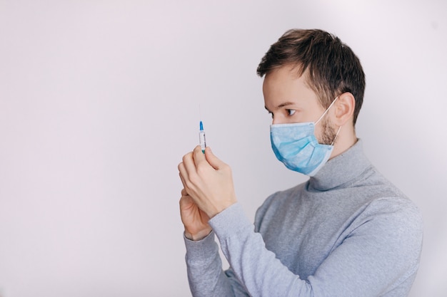 De mens met spuit treft voor injectie voorbereidingen. Professionele arts met medische spuit in handen klaar voor injectie. Doctor in de medische masker houdt spuit met vaccin.