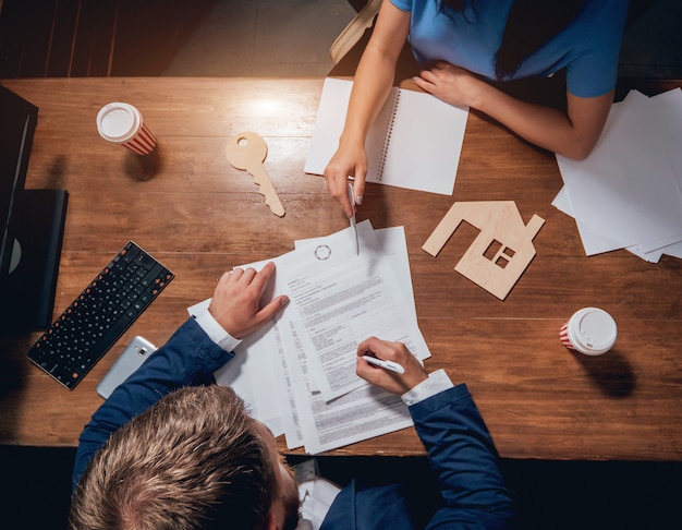 De mens ondertekent een huisverzekeringspolis op huisleningen. makelaar met klant voor contractondertekening.