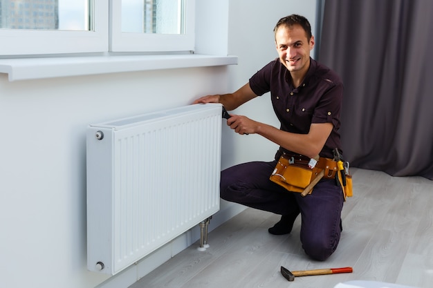 De mens repareert de radiatorbatterij in de kamer. Onderhoud reparatie werkt renovatie in de flat. Restauratie verwarming. Moersleutel in handen