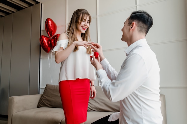 De mens stelt zijn verloofde voor met ring- en hartvormige rode ballonnen