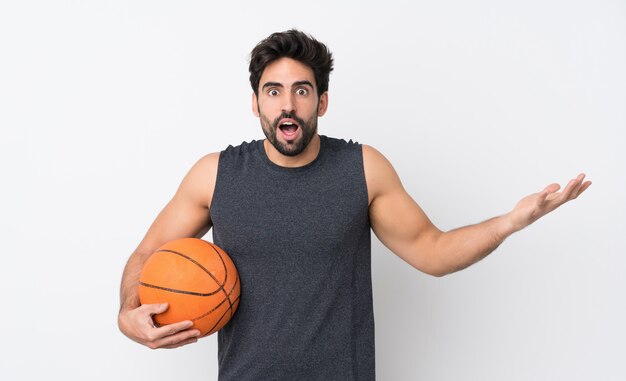 De mens van de basketbalspeler met baard over geïsoleerde witte muur met geschokte gelaatsuitdrukking