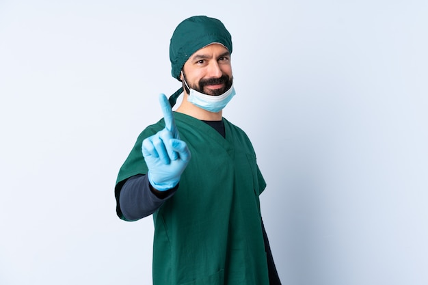 De mens van de chirurg in groen uniform over muur die en een vinger toont opheft