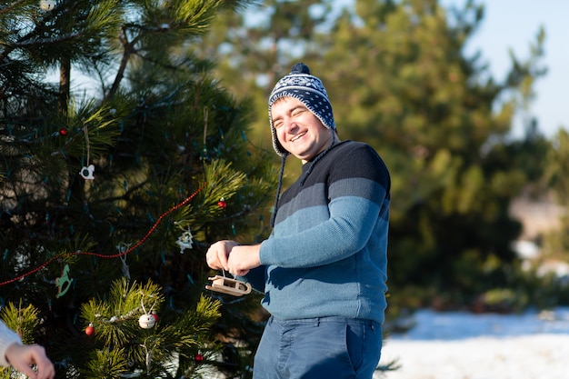 De mens verfraait met een decoratief stuk speelgoed en slinger een groene kerstboom op straat in de winter in het bos