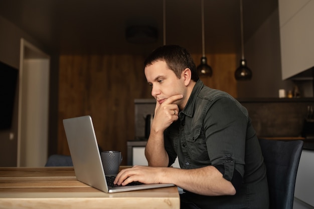 De mens werkt binnen aan laptop, bij het bureau in de keukenruimte. Werk vanuit huis