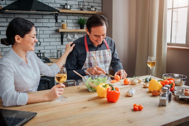 De mens zit bij lijst in keuken en sneed groenten voor salade.