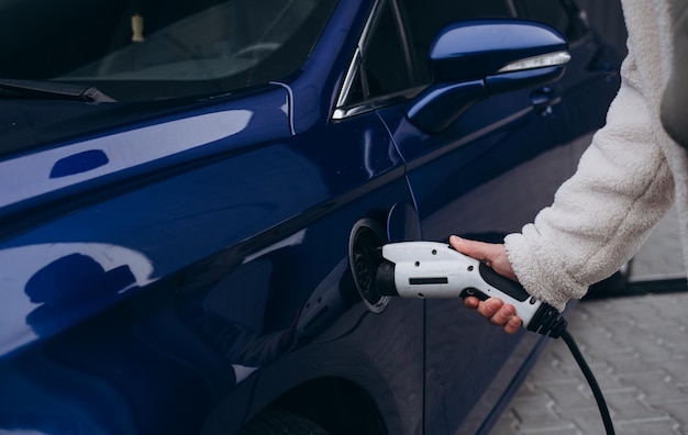 De menselijke hand houdt het elektrische auto laden verbindt met elektrische auto