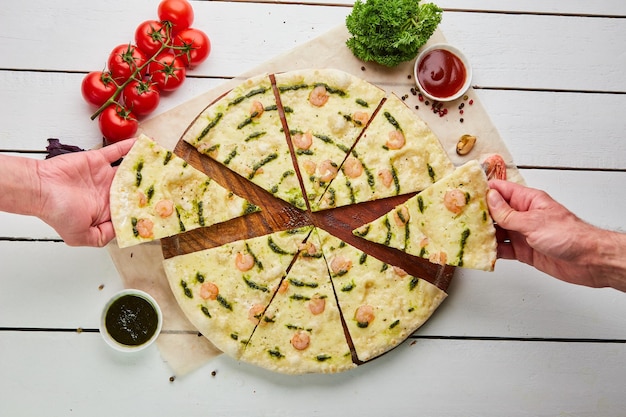 De menselijke hand neemt Vers gebakken smakelijke pizza met garnalen en mozzarella kaas geserveerd op houten achtergrond met tomatensaus en kruiden Voedsel levering concept Restaurant menu
