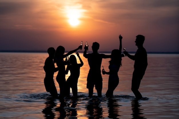 De mensen dansen op het strandfeest 's avonds tegen de zonsondergang