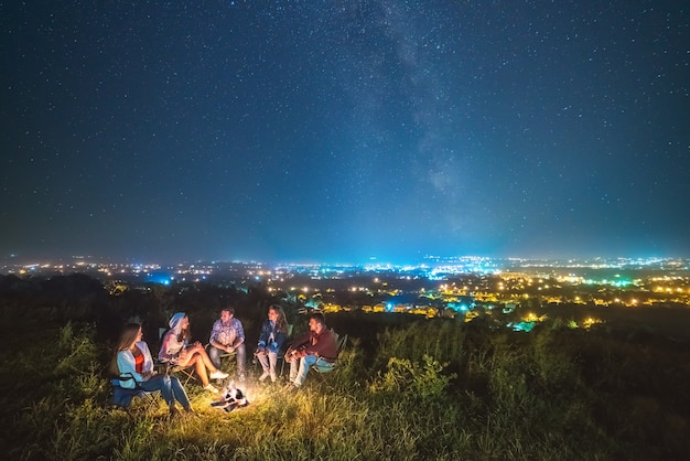 De mensen rusten in de buurt van een vreugdevuur op de sterrenhemel achtergrond. avond nacht tijd