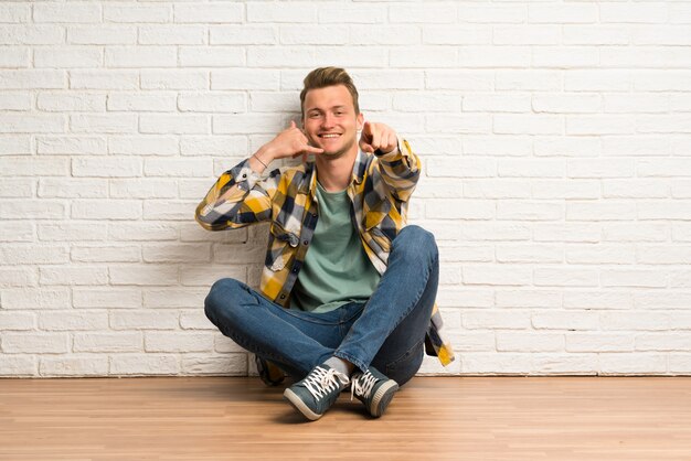 De mensenzitting van de blonde op de vloer die telefoongebaar maakt en voorzijde richt