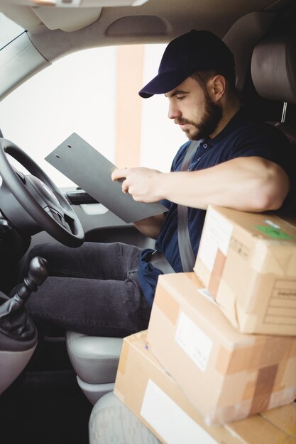 De mensenzitting van de levering in zijn bestelwagen terwijl het schrijven op klembord