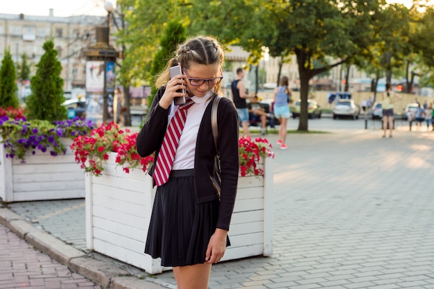 De middelbare schoolstudent van de tiener op stadsstraat die op telefoon spreekt