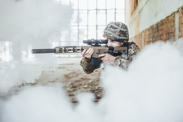 De militaire soldaat in uniform houdt een modern geweer in zijn handen, hij mikt in de rook