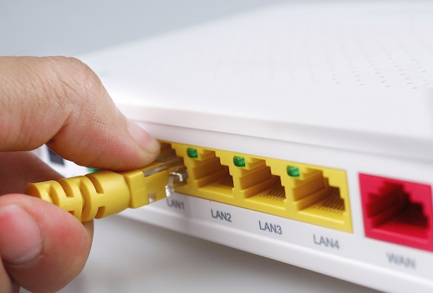 Foto de modemhub van internet met hand die gele kabel houdt die geïsoleerde witte achtergrond verbindt