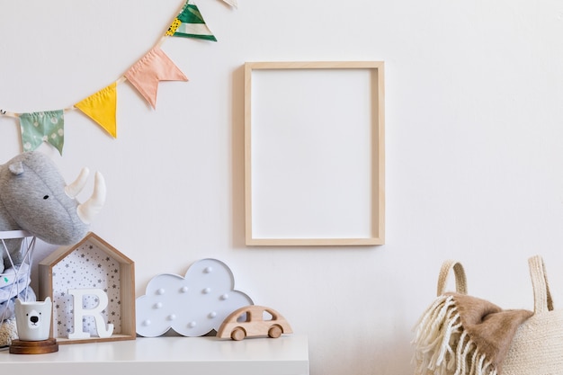 De moderne scandinavische pasgeboren babykamer met mock-up fotolijst, houten auto, knuffels en wolken. Hangende katoenen vlaggen en witte sterren. Minimalistisch en gezellig interieur met witte muren.