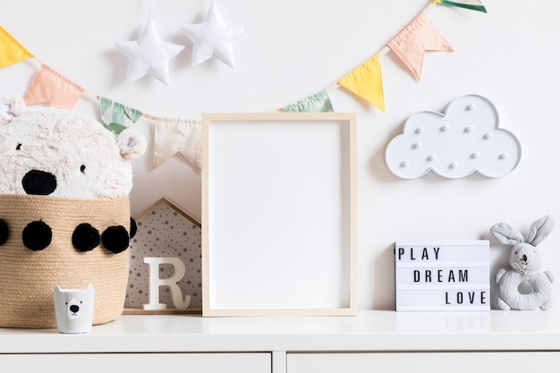 De moderne scandinavische pasgeboren babykamer met mock-up fotolijst, houten auto, knuffels en wolken. Hangende katoenen vlaggen en witte sterren. Minimalistisch en gezellig interieur met witte muren.