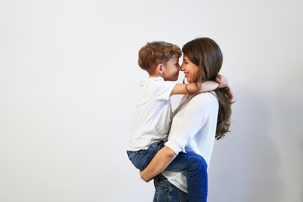 De moeder die haar preteen zoon houdt glimlacht en onderzoekend zijn oog