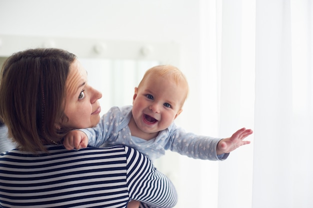 De moeder draagt schouder lachende babyjongen thuis