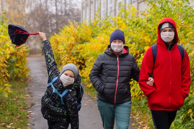 De moeder met twee zoons op straat met beschermende maskers, lopend