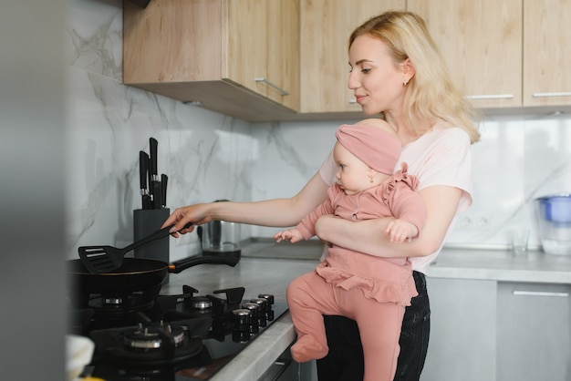 De moeder van een vrouw met een baby kookt het eten in een pan op het fornuis