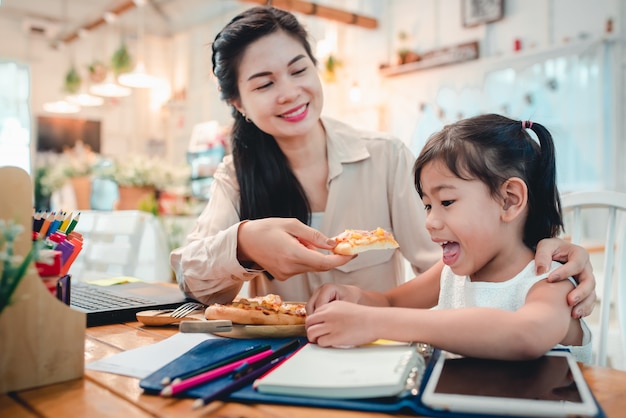 De moeder zorgt voor pizzavoedsel voor haar kind dat huiswerk maakt en thuis online studeert