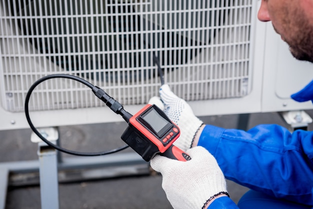 De monteur controleert met een digitale camera de verstopping van de warmtewisselaar