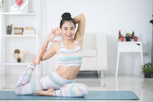 De mooie Aziatische sportenvrouw voert thuis de oefeningen uit. Yoga