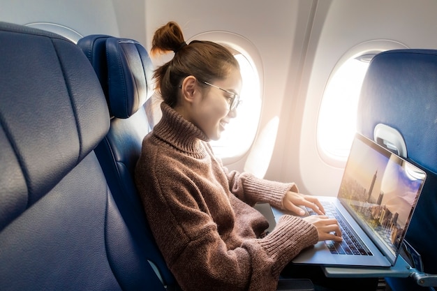 De mooie Aziatische vrouw werkt met laptop in vliegtuig