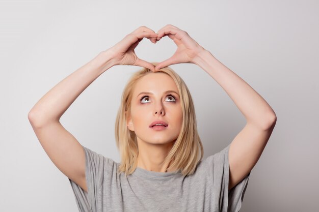 Foto de mooie blondevrouw toont liefdegebaar op witte muur