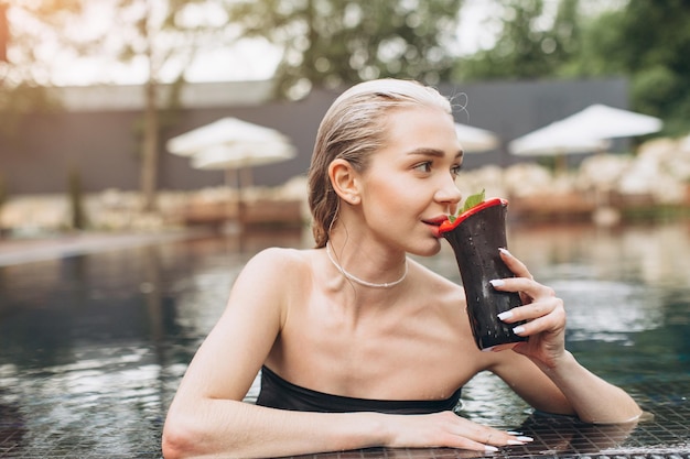 De mooie en stijlvolle blonde vrouw ontspannen in het zwembad met een cocktail in de zomer