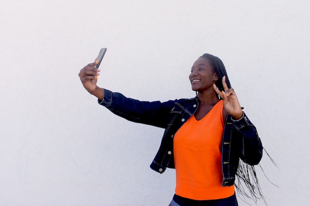 De mooie en vrolijke Afrikaanse Amerikaan neemt een selfie op een witte muur