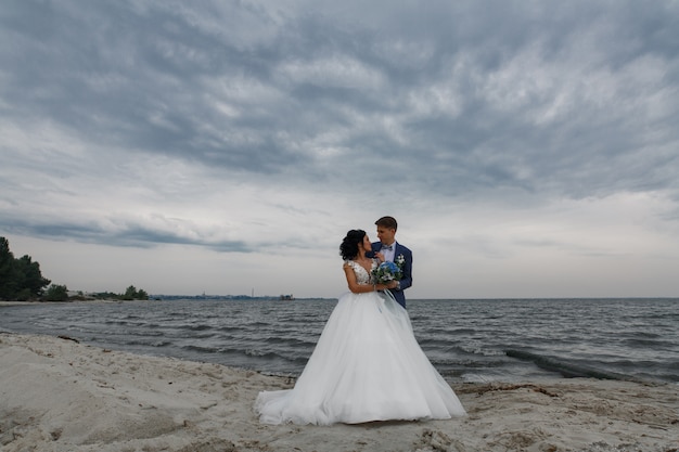 De mooie gelukkige bruid en de bruidegom van het huwelijkspaar bij huwelijksdag in openlucht bij strand